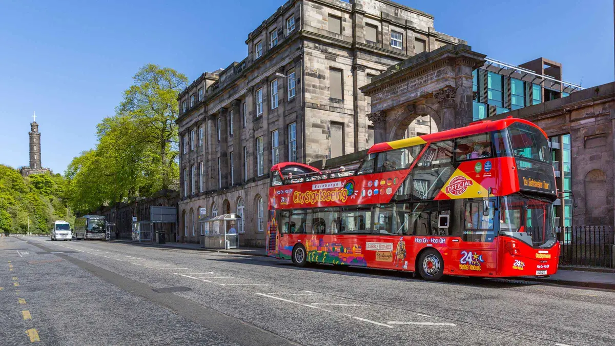 Red open-top City Sightseeing bus below Castle Rock on a hop-on hop-off bus tour of Edinburgh